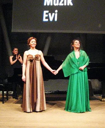 Ferzan in a green gown holding hands on stage with a woman in a striped gown