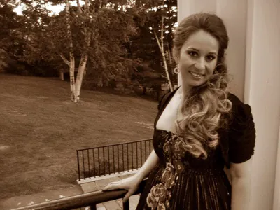 Sepia photograph of Ferzan in a dark dress, smiling on a terrace with trees behind her